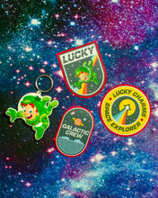 The 3 Lucky Charms™ Galactic Patches with keychain in front of an outer space background.
