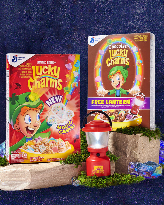 Red Lucky Charms™ Coleman® brand lantern in front of 2 cereal boxes. 